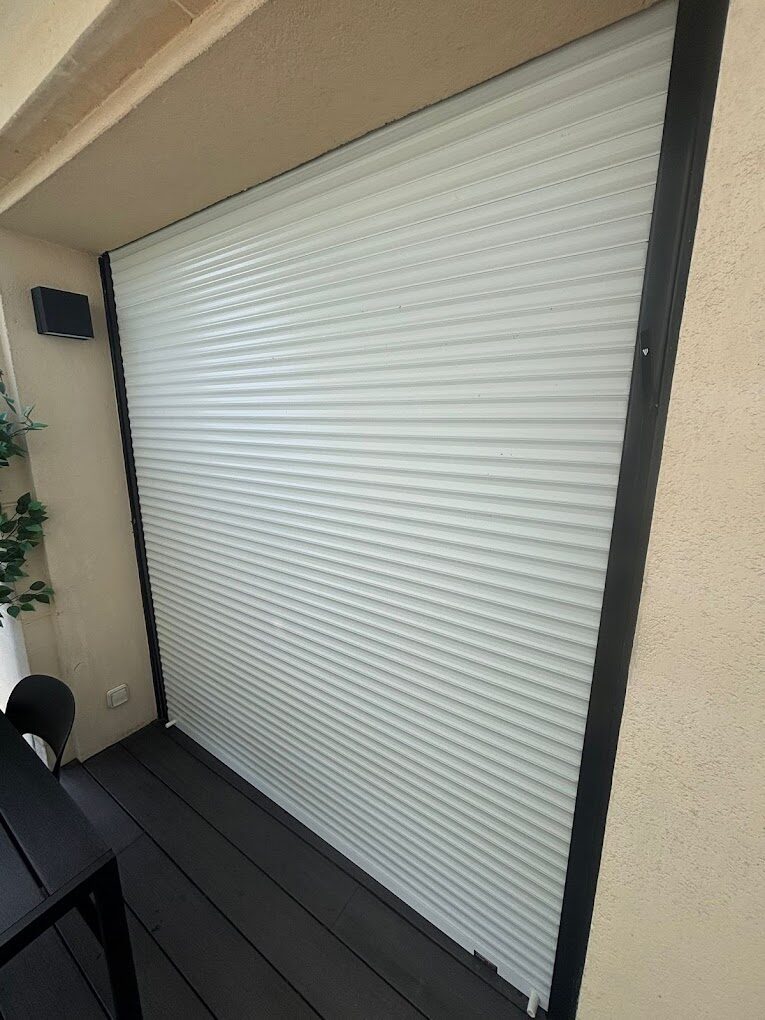 Volet roulant blanc fermé, posé sur une terrasse à sol sombre